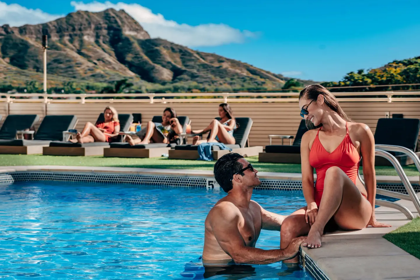 Guests relaxing by the pool with Diamond Head behind them at Queen Kapiolani Hotel.