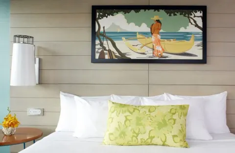 A close view of a king bed with tropical artwork at Queen Kapiolani Hotel.