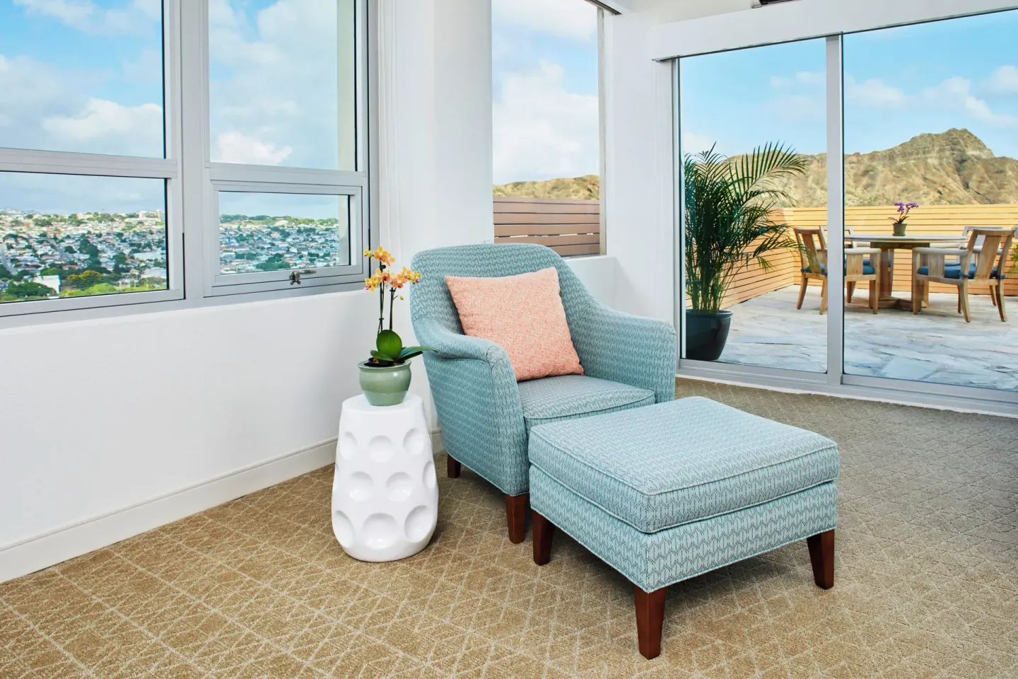 Blue armchair and ottoman beside windows and a terrace at Queen Kapiolani Hotel.
