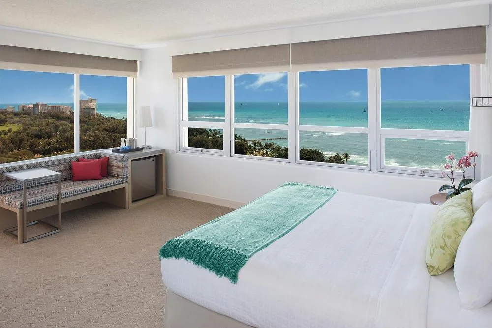 Premier Ocean View Balcony room with king bed and ocean-facing windows at Queen Kapiolani Hotel.