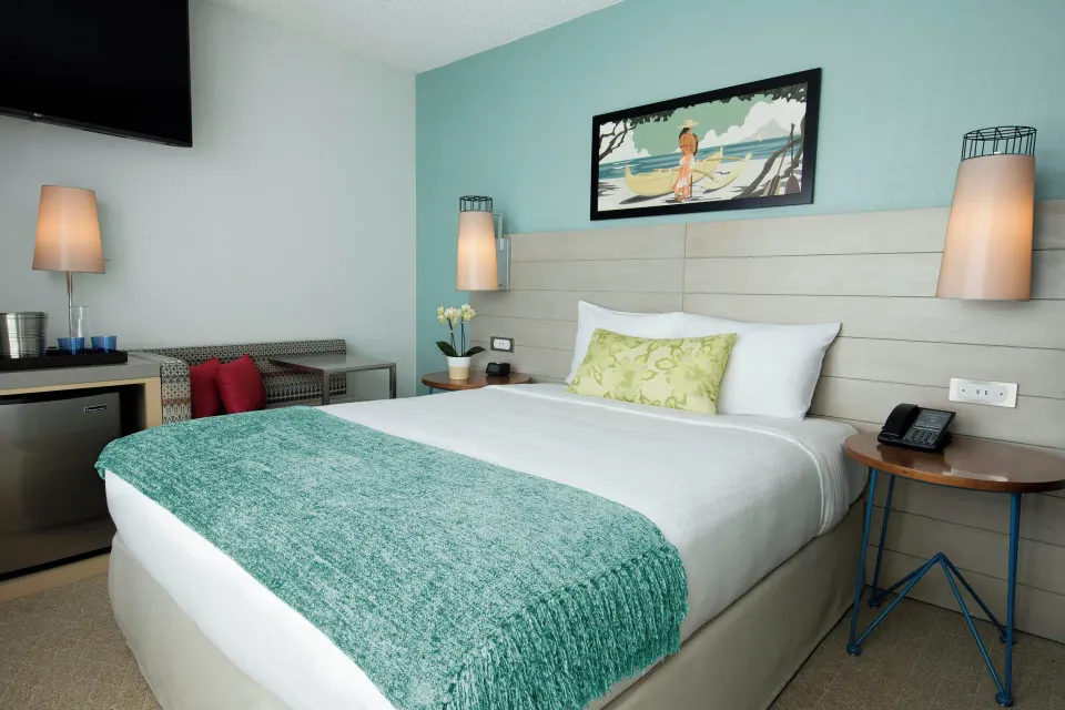 Studio City View king bed, bench, TV, and minibar area at Queen Kapiolani Hotel.
