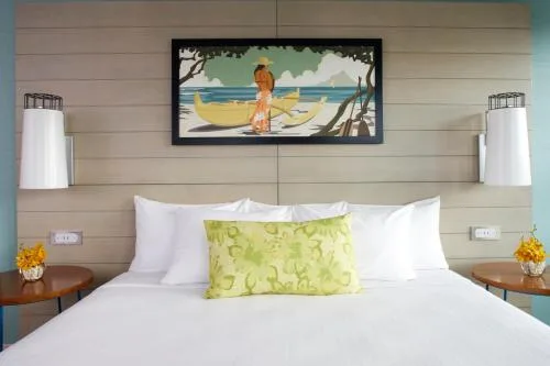 Studio king bed with beach artwork and side tables at Queen Kapiolani Hotel.