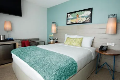 Studio king room with aqua wall, bedside lamp, phone, and TV at Queen Kapiolani Hotel.