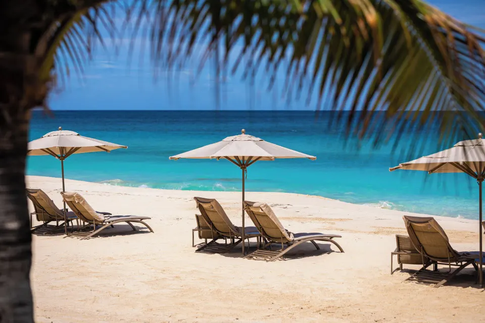Beach loungers and umbrellas on white sand with turquoise water at Quintessence Hotel