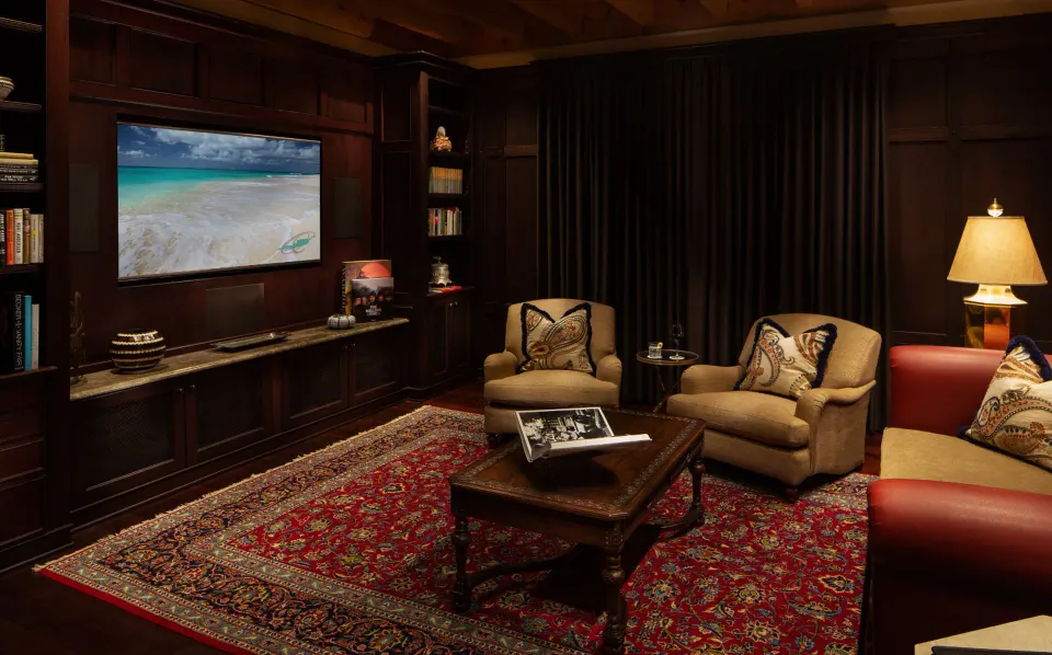 Cozy dark-wood media room with armchairs and a wall-mounted TV at Quintessence Hotel