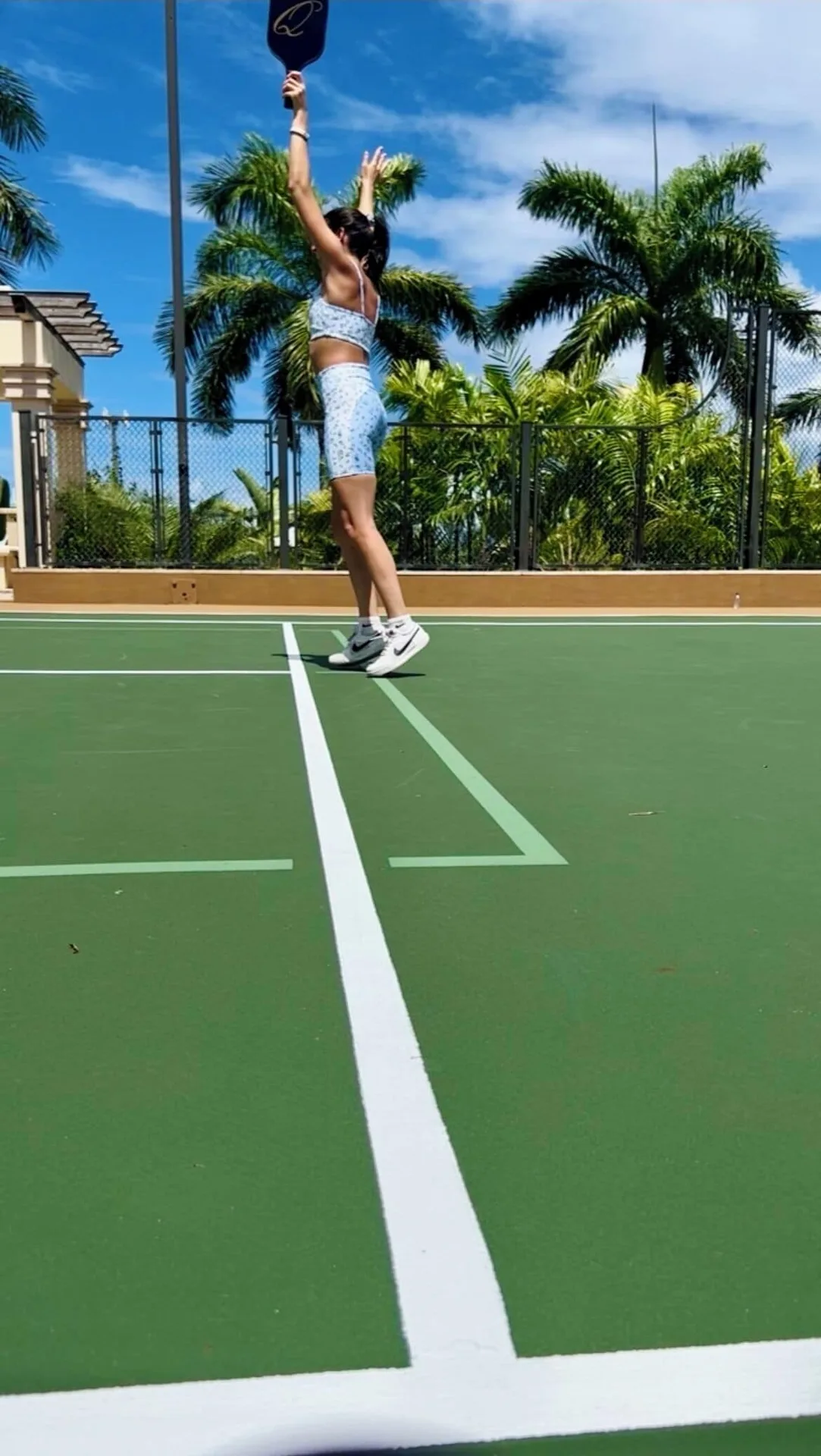 Guest serving a ball on the court under palm trees at Quintessence Hotel.