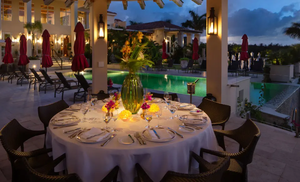 Poolside evening dining table set beside illuminated resort pool at Quintessence Hotel
