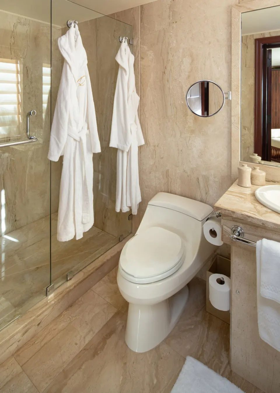 Marble bathroom with toilet, glass shower and hanging robes in a Garden View Long Bay Standard Suite at Quintessence Hotel