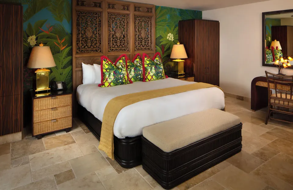 Front view of king bed with tropical cushions and bedside lamps in a Garden View Long Bay Standard Suite at Quintessence Hote
