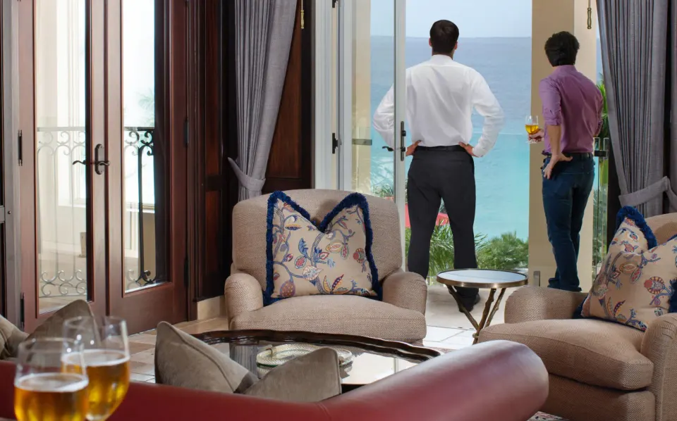 Seating area opening to a balcony with two men looking out at Quintessence Hotel