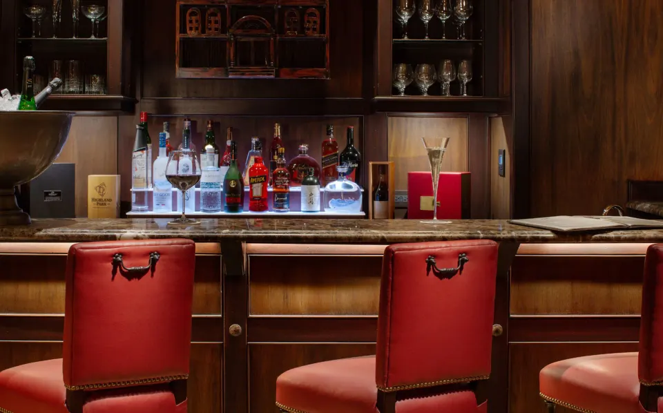 Close-up of a stocked minibar and three red leather bar stools at Quintessence Hotel