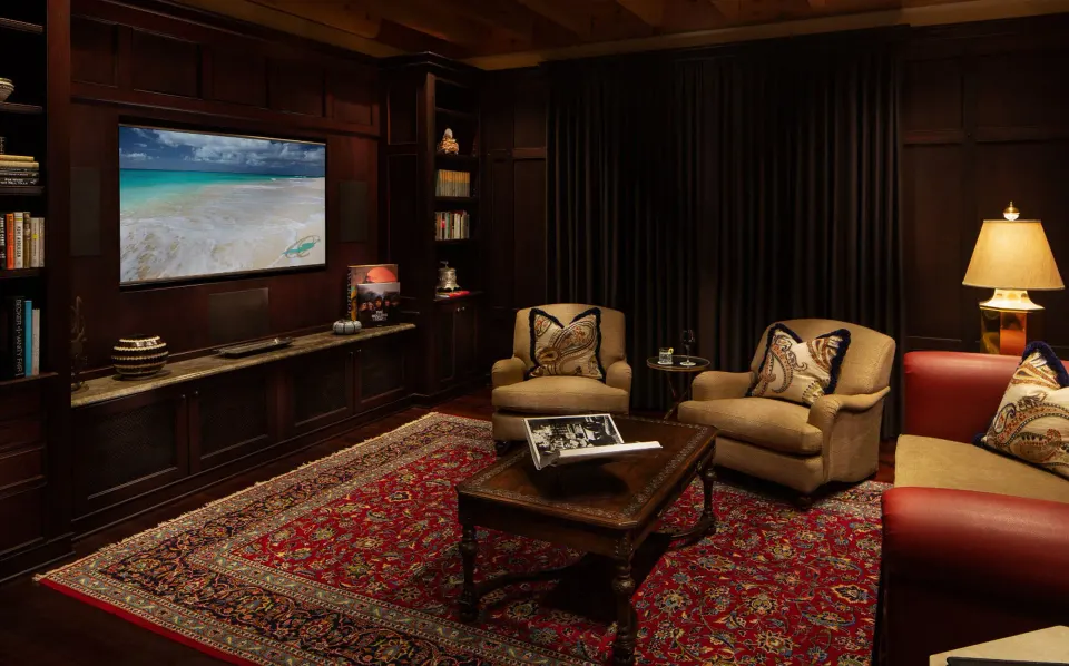 Cozy media room with armchairs, rug and wall-mounted screen at Quintessence Hotel