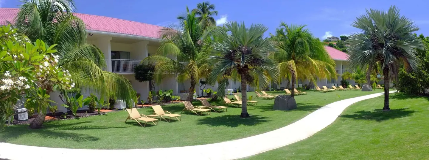 Curving walkway, palms, and lounge chairs on the lawn at Radisson Grenada Beach Resort.
