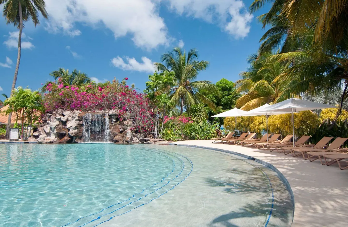 Rock waterfall and shaded loungers beside the pool at Radisson Grenada Beach Resort.