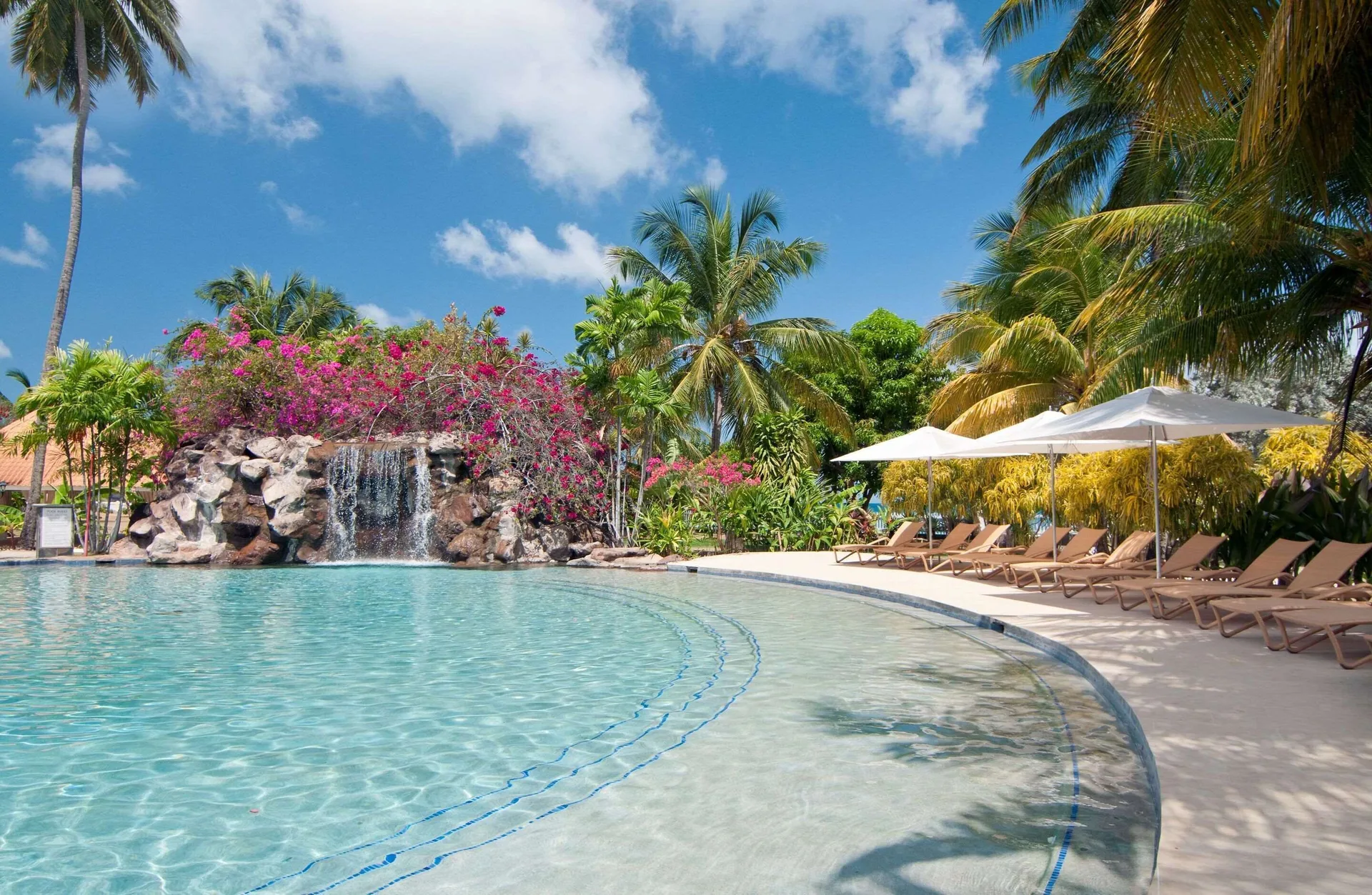 Rock waterfall and shaded loungers beside the pool at Radisson Grenada Beach Resort.
