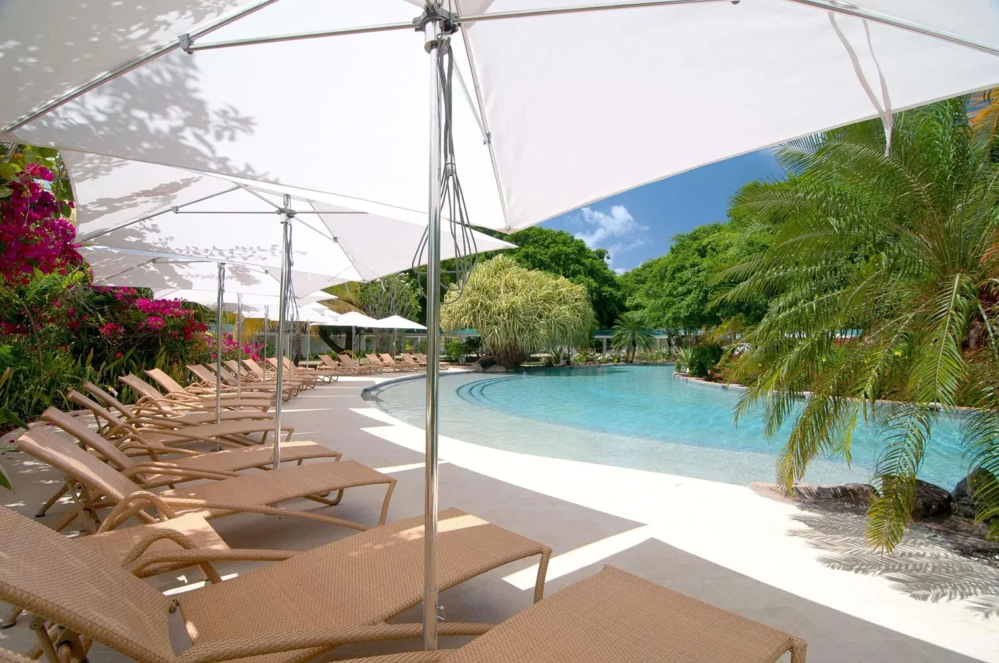 Poolside loungers under white umbrellas beside tropical landscaping at Radisson Grenada Beach Resort.