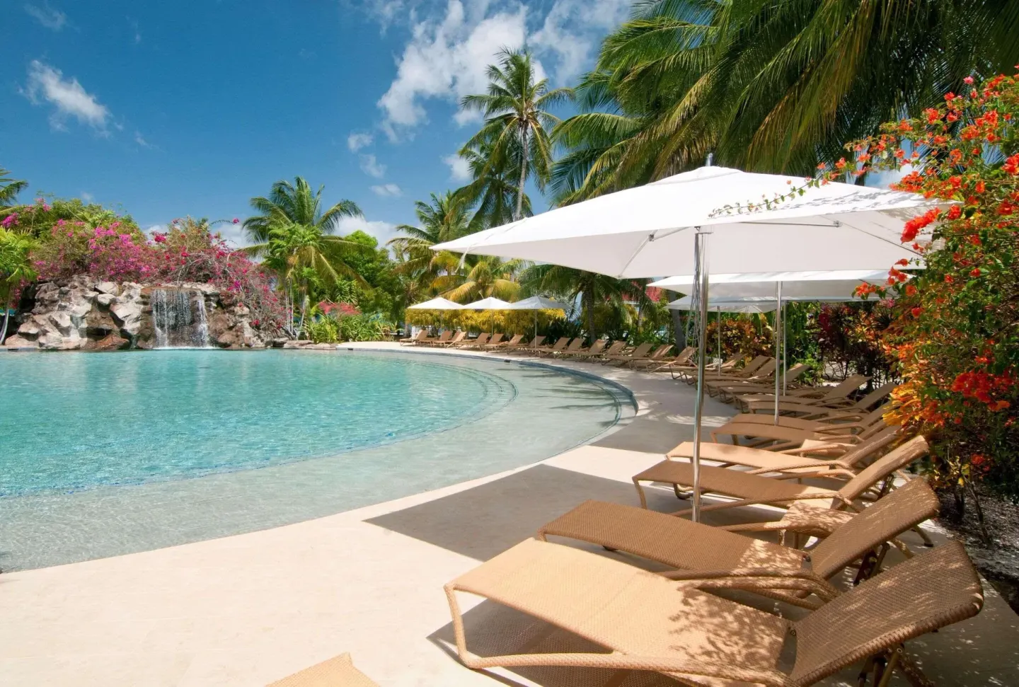 Curved resort pool with loungers, umbrellas and waterfall at Radisson Grenada Beach Resort.