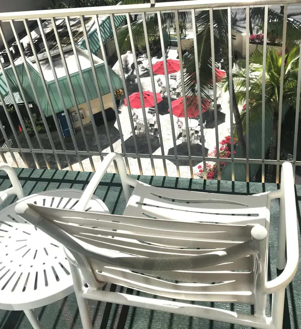 Balcony seating at Ramada Plaza Waikiki overlooking red umbrellas, palms, and the courtyard below.