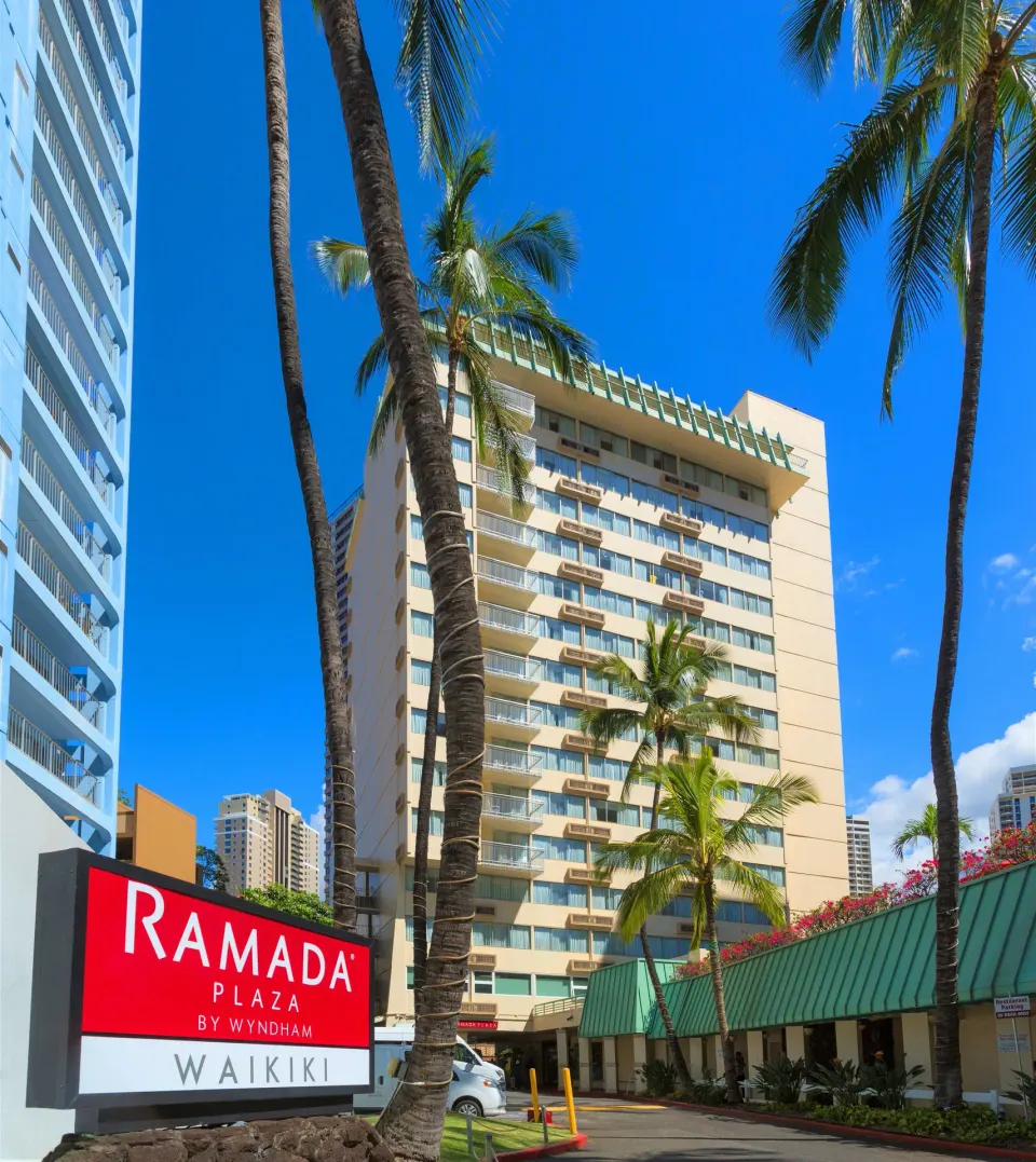 Ramada Plaza Waikiki exterior tower and sign framed by palm trees.