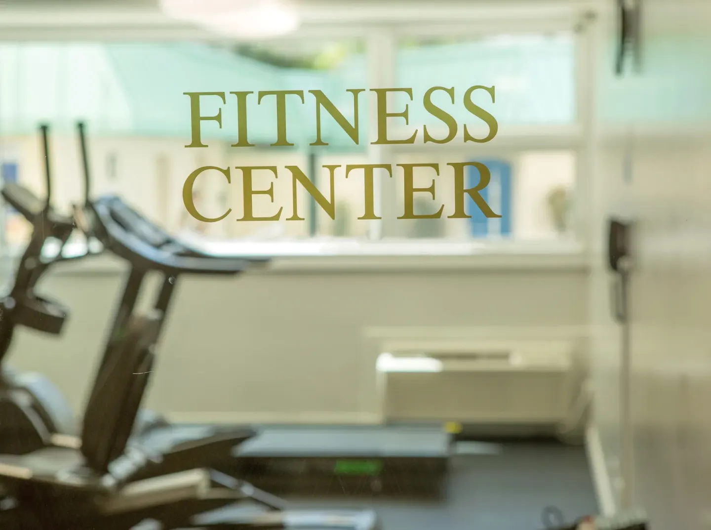 Fitness Center lettering on glass with exercise equipment behind it at Ramada Plaza Waikiki.