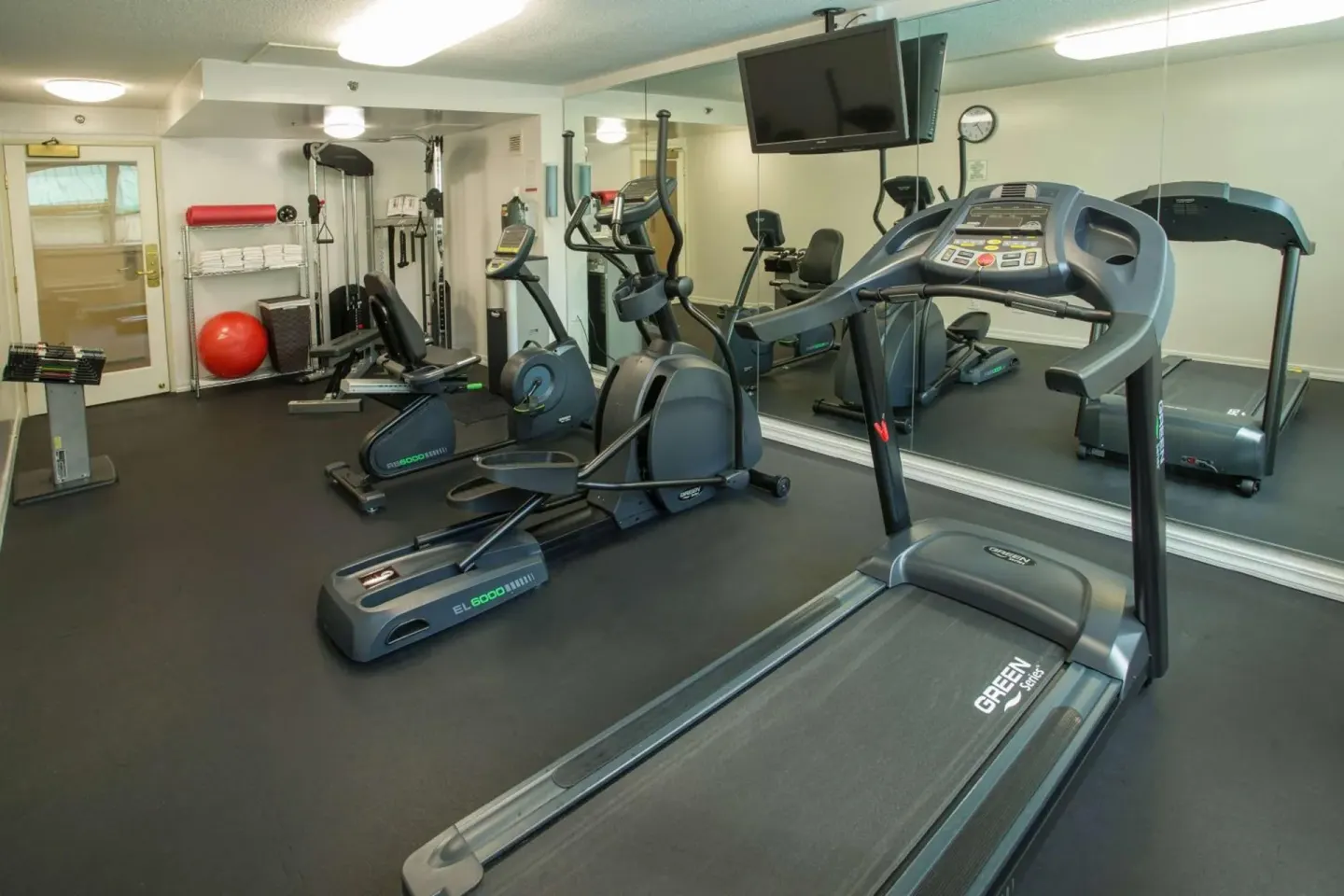 Fitness room with treadmills, ellipticals, weights, mirrors, and a wall TV at Ramada Plaza Waikiki.