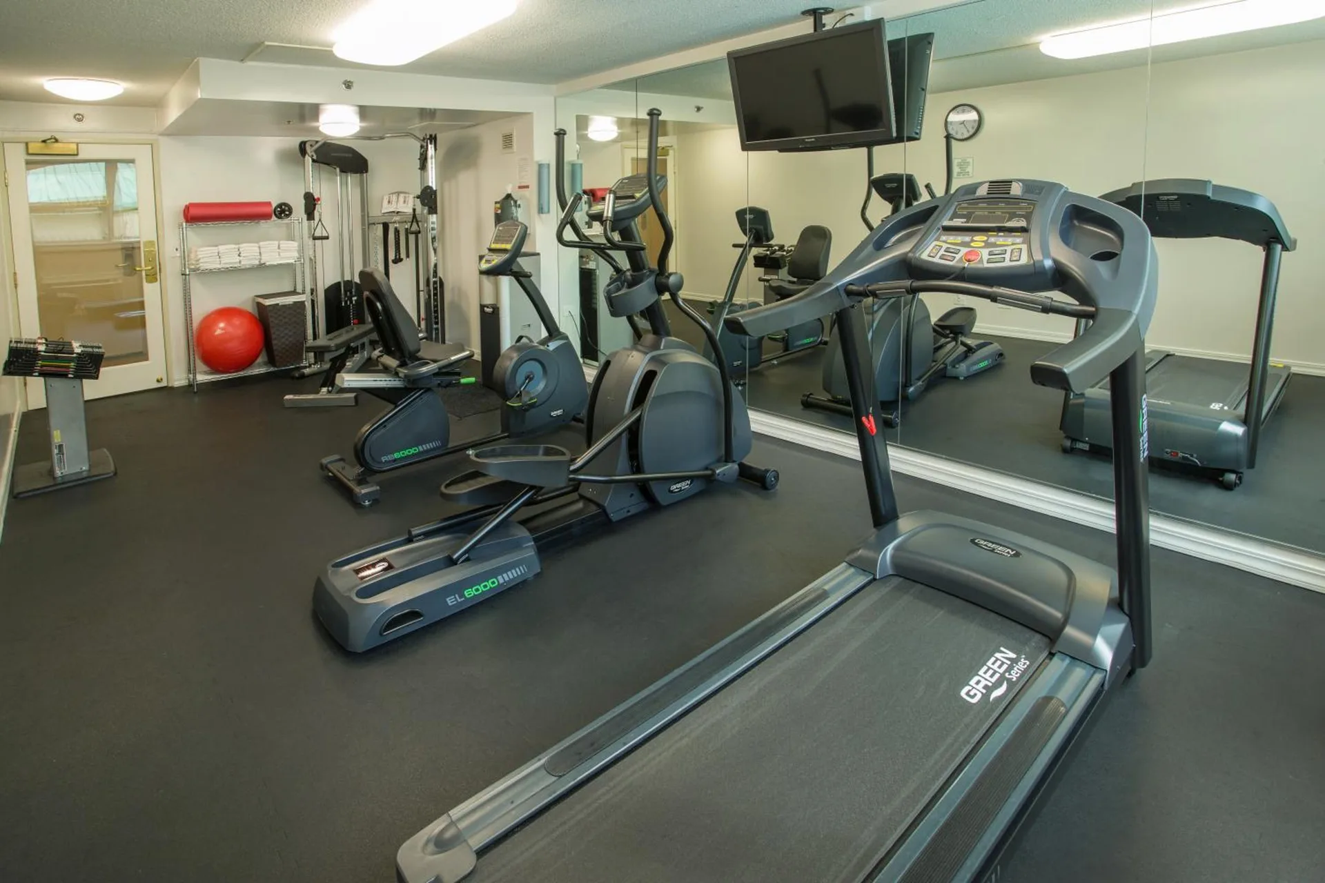 Fitness room with treadmill, elliptical machines, weights, and mirrors at Ramada Plaza Waikiki.