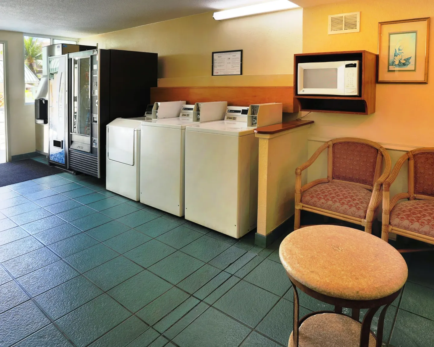 Guest laundry area with washers, dryers, vending machines, and chairs at Ramada Plaza Waikiki.