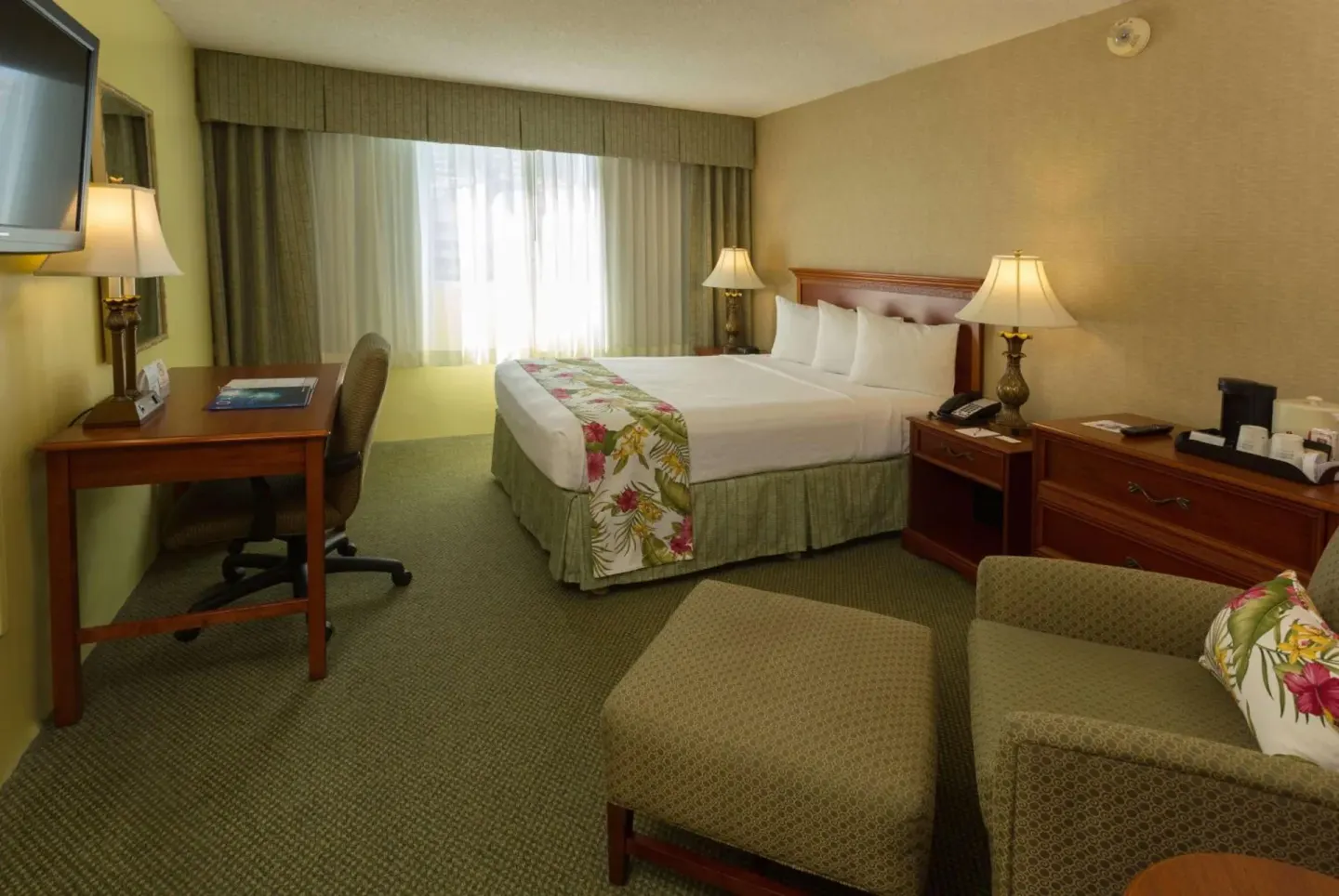 King guest room with desk, lounge chair, and ottoman at Ramada Plaza Waikiki.