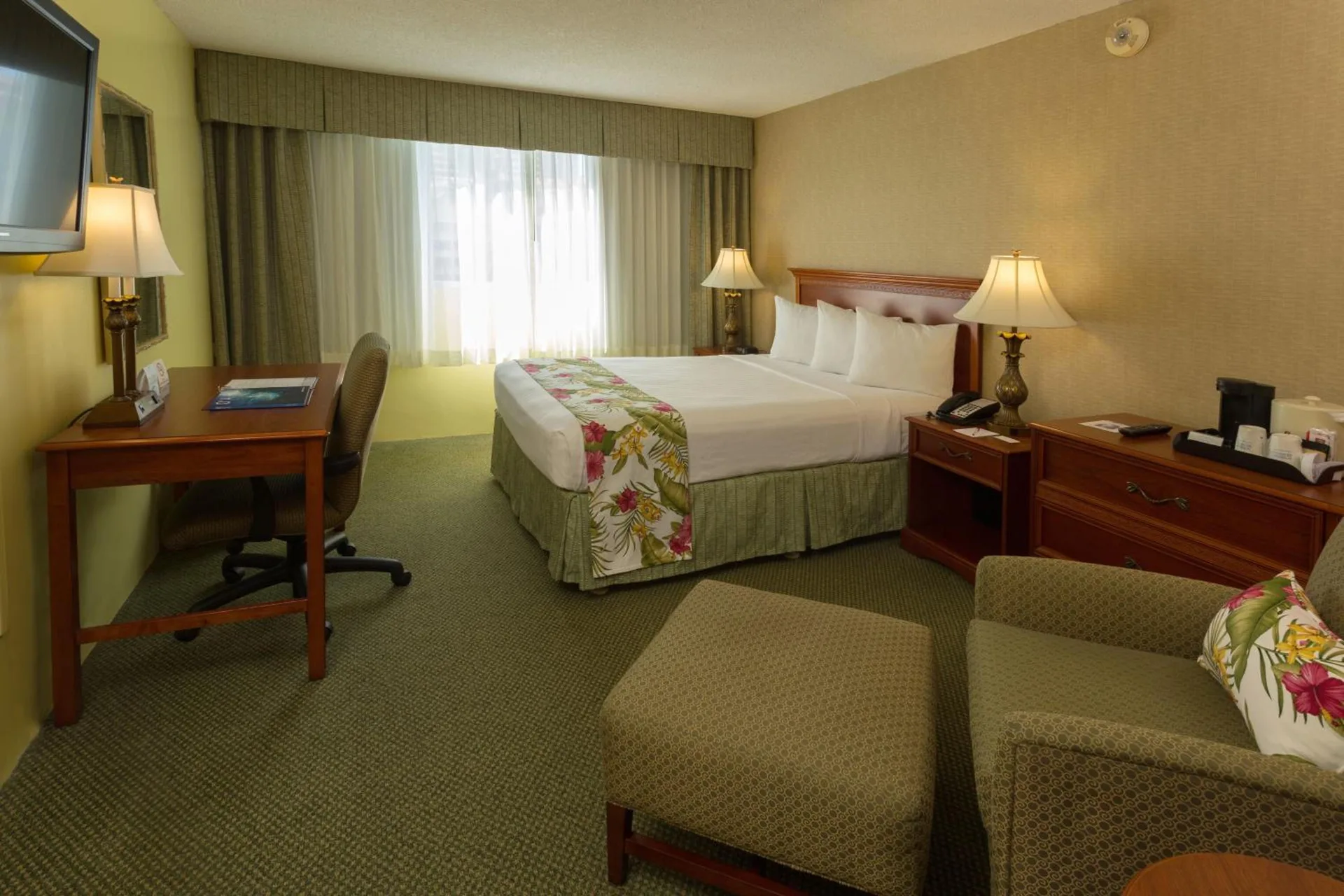 King guest room with desk, armchair, ottoman, and window at Ramada Plaza Waikiki.