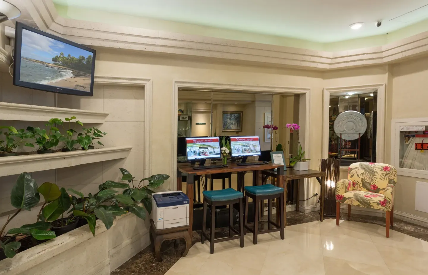 Lobby computer station with plants, stools, and a floral chair at Ramada Plaza Waikiki.