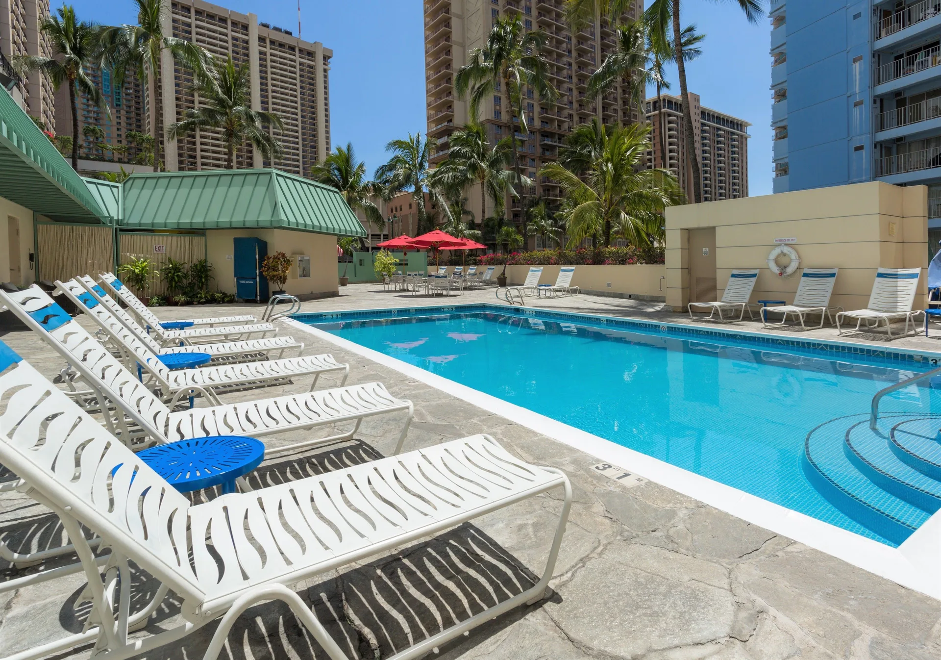 Outdoor pool with lounge chairs and palms at Ramada Plaza Waikiki.