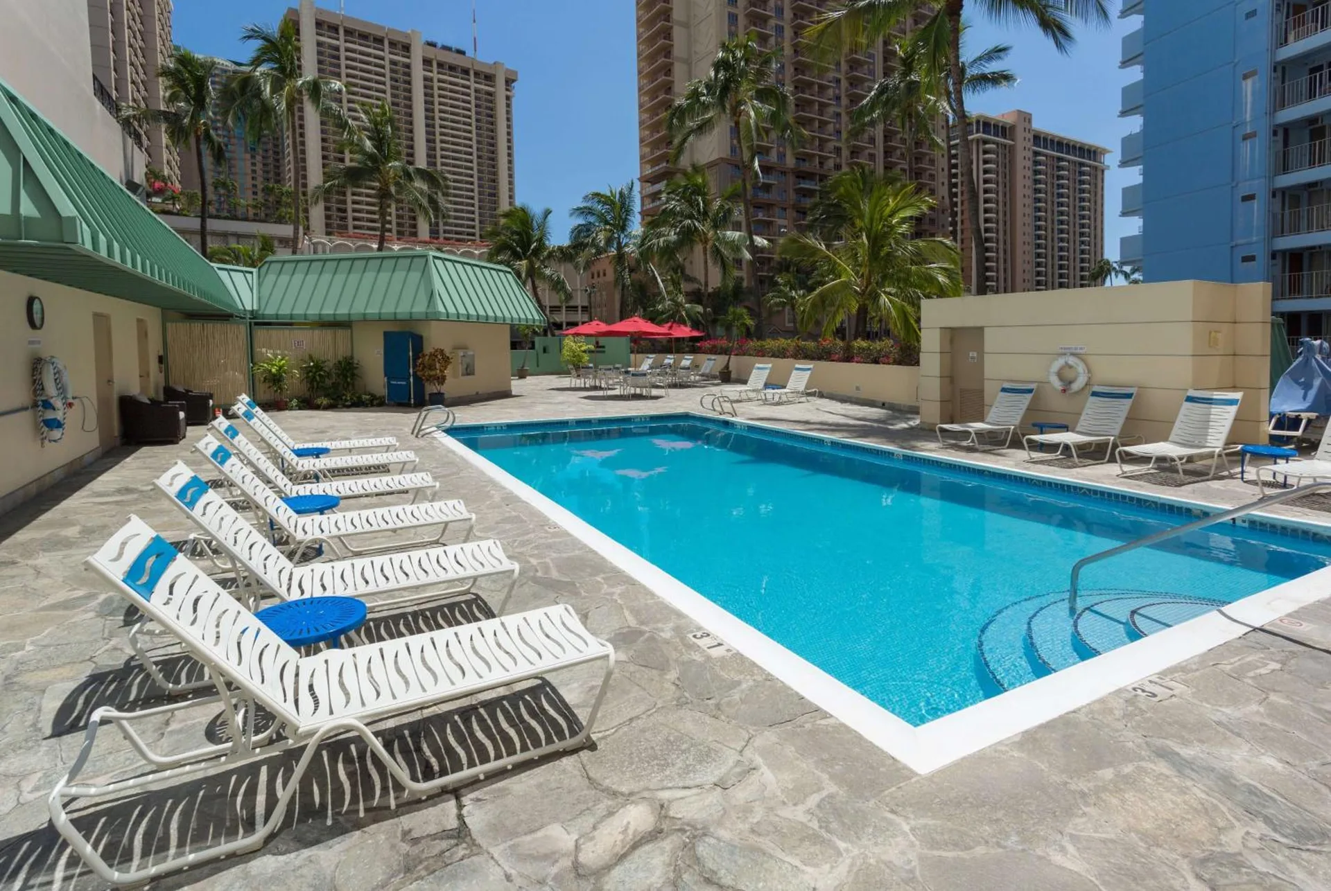 Outdoor swimming pool with lounge chairs and city towers at Ramada Plaza Waikiki.