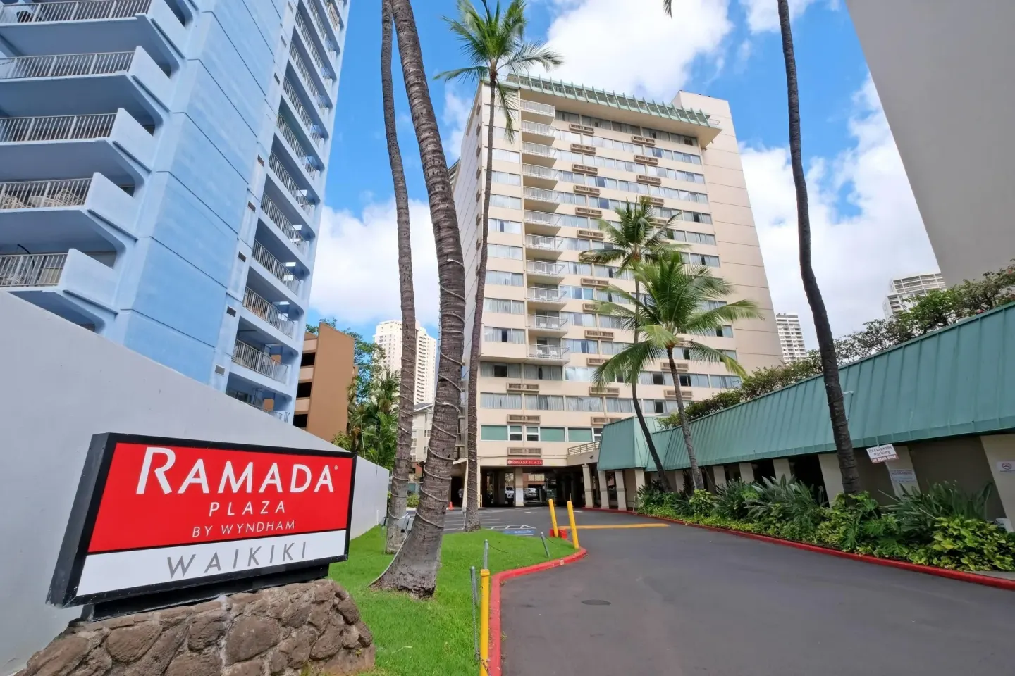 Ramada Plaza Waikiki roadside sign beside the driveway, palms, and hotel tower.