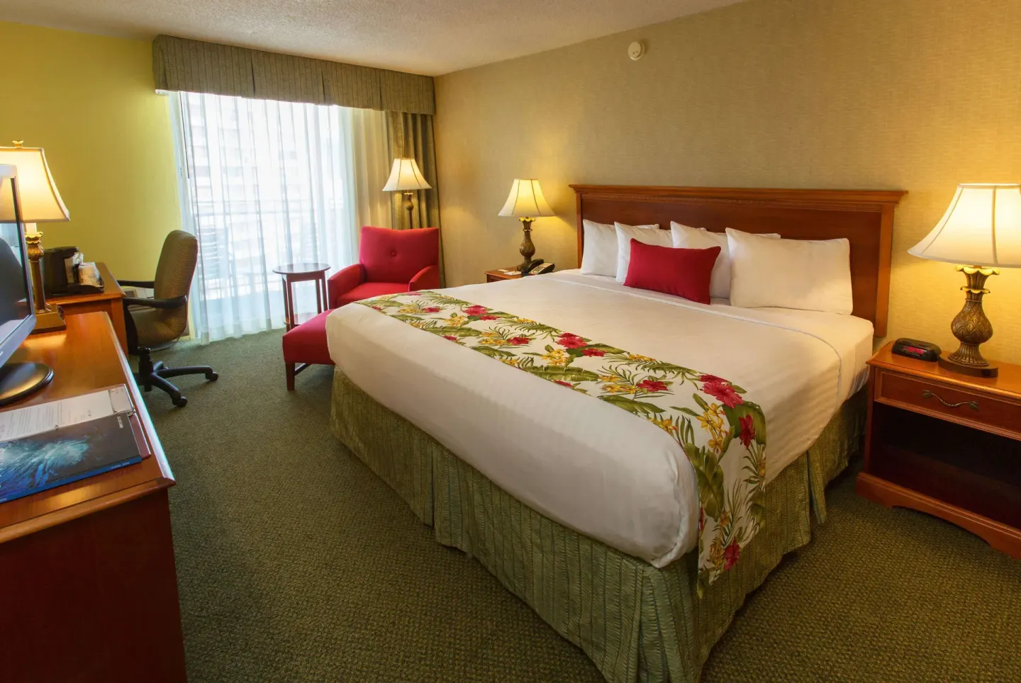 King bed balcony room with desk, red chair, and lamps at Ramada Plaza Waikiki.