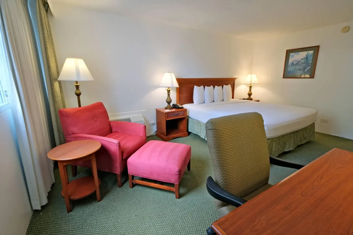 King bed guest room with red chair, ottoman, and desk at Ramada Plaza Waikiki.