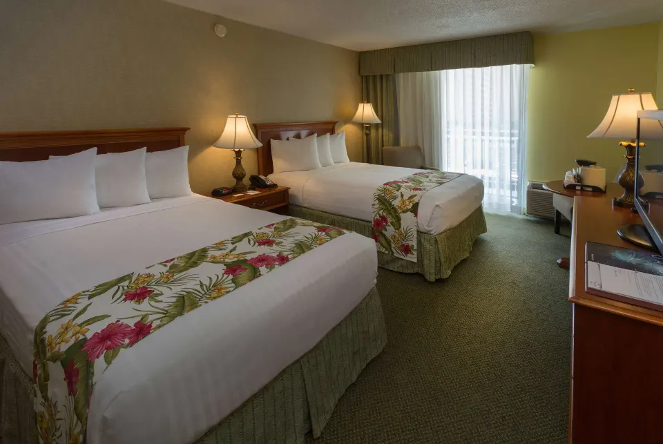 Two-bed balcony guest room with desk and lamps at Ramada Plaza Waikiki.
