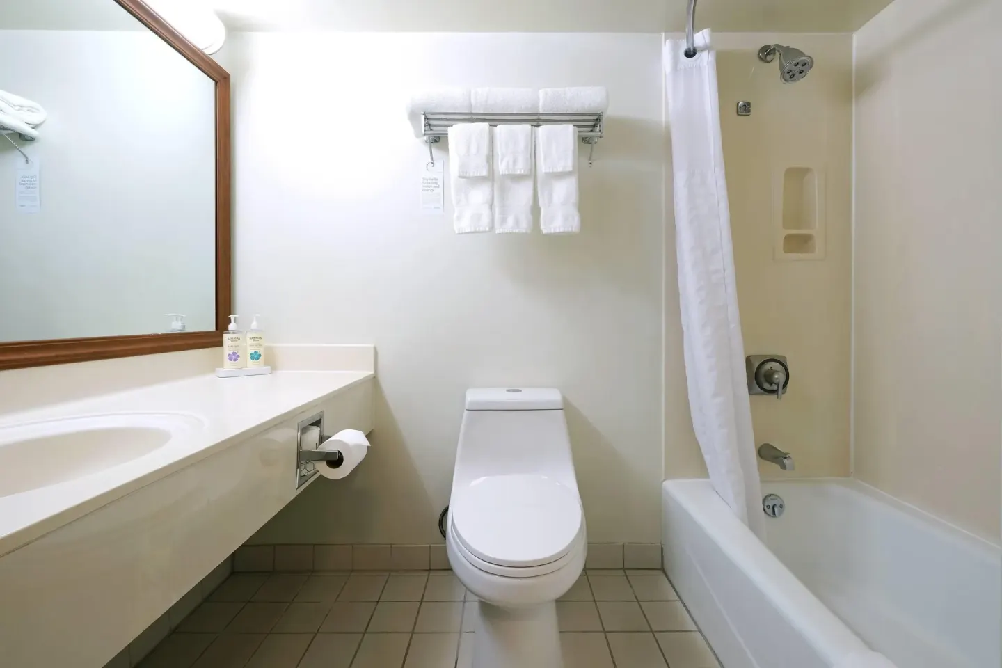 Standard Room bathroom at Ramada Plaza Waikiki with vanity, toilet, towels, and tub shower.