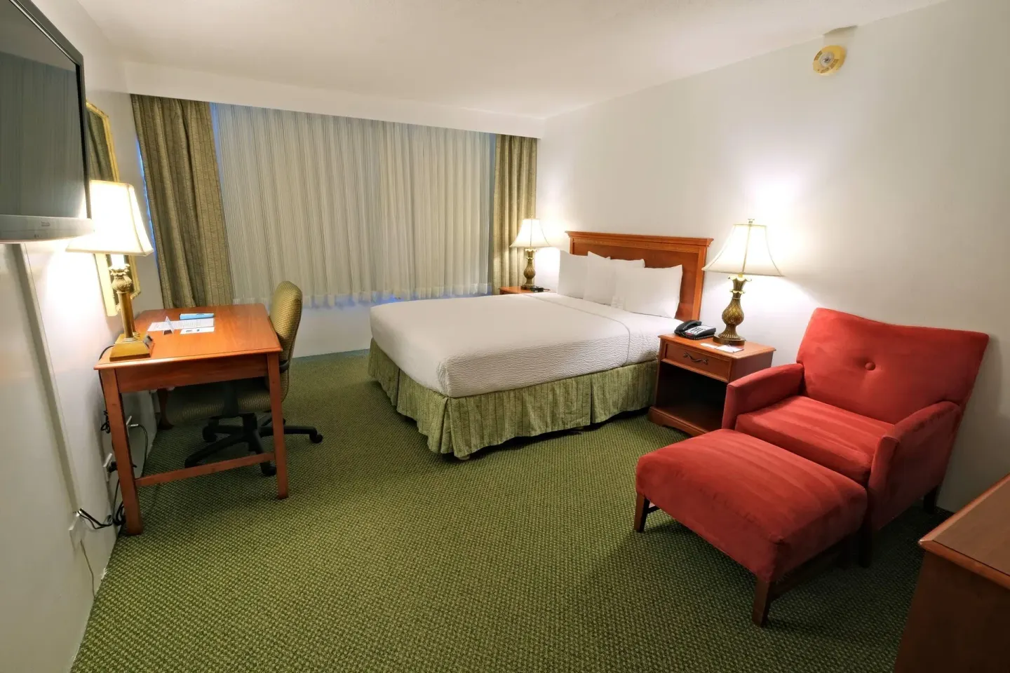 Standard Room with one bed, desk, red lounge chair and ottoman at Ramada Plaza Waikiki.