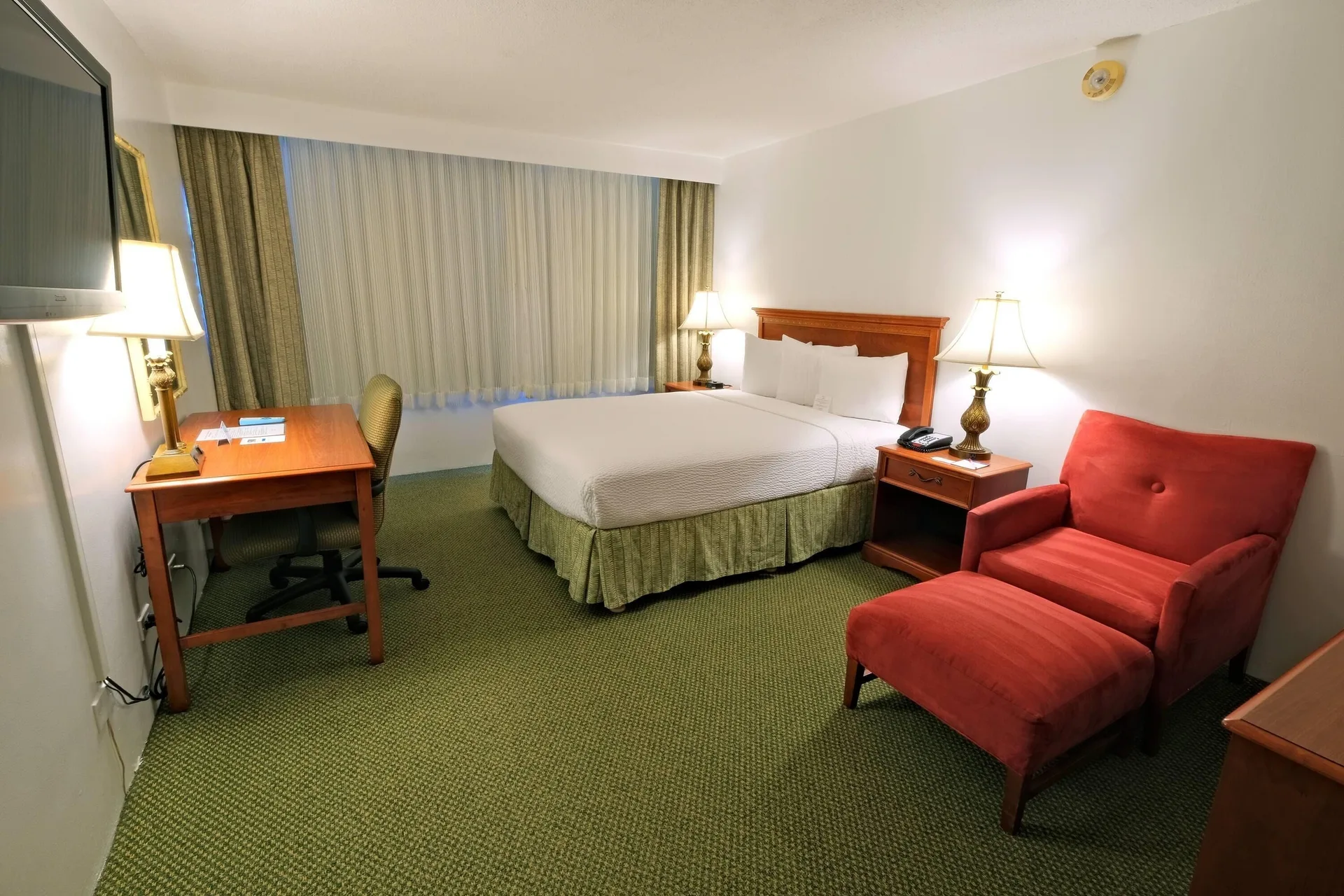 Standard Room at Ramada Plaza Waikiki with king bed and red lounge chair in Waikiki, Honolulu.