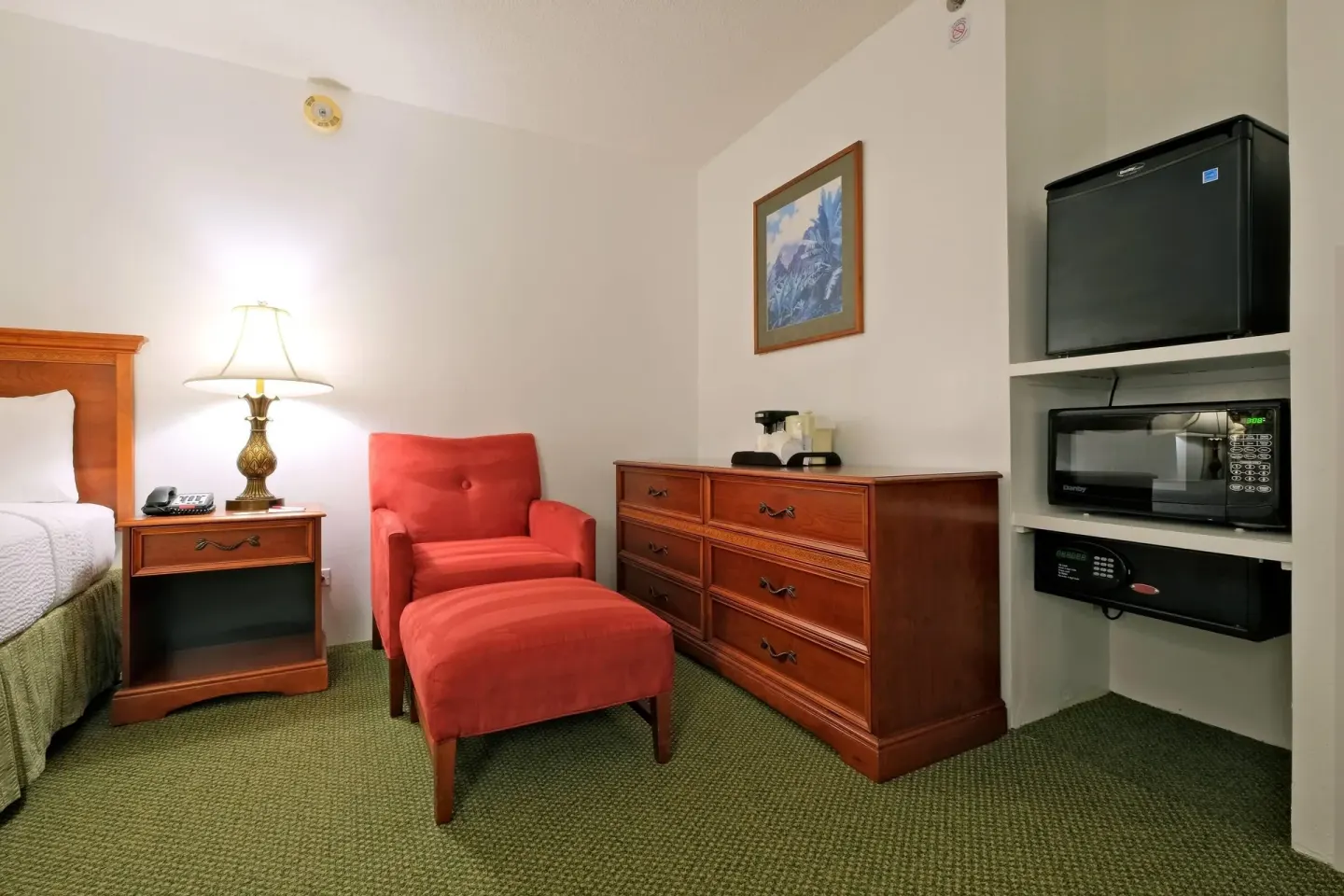 Standard Room seating area with red chair, dresser, mini fridge, microwave and safe at Ramada Plaza Waikiki.