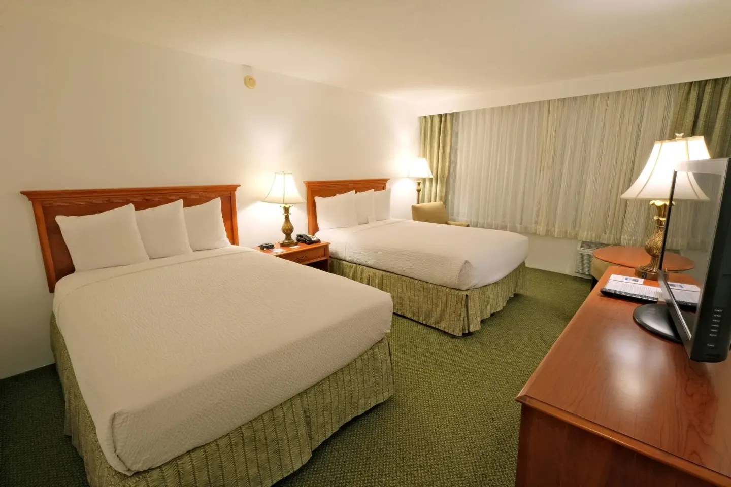Standard Room with two double beds, TV dresser and wide curtained window at Ramada Plaza Waikiki.