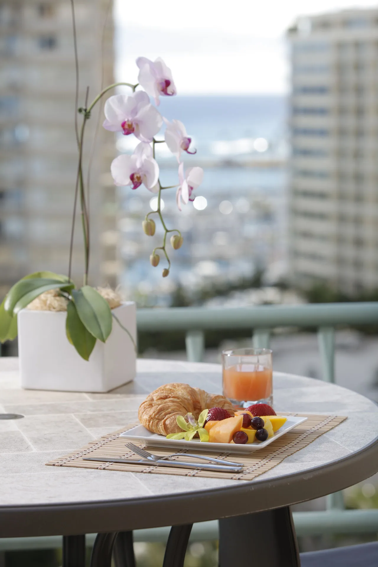 Balcony table with breakfast and orchid outside a studio suite at Ramada Plaza Waikiki.