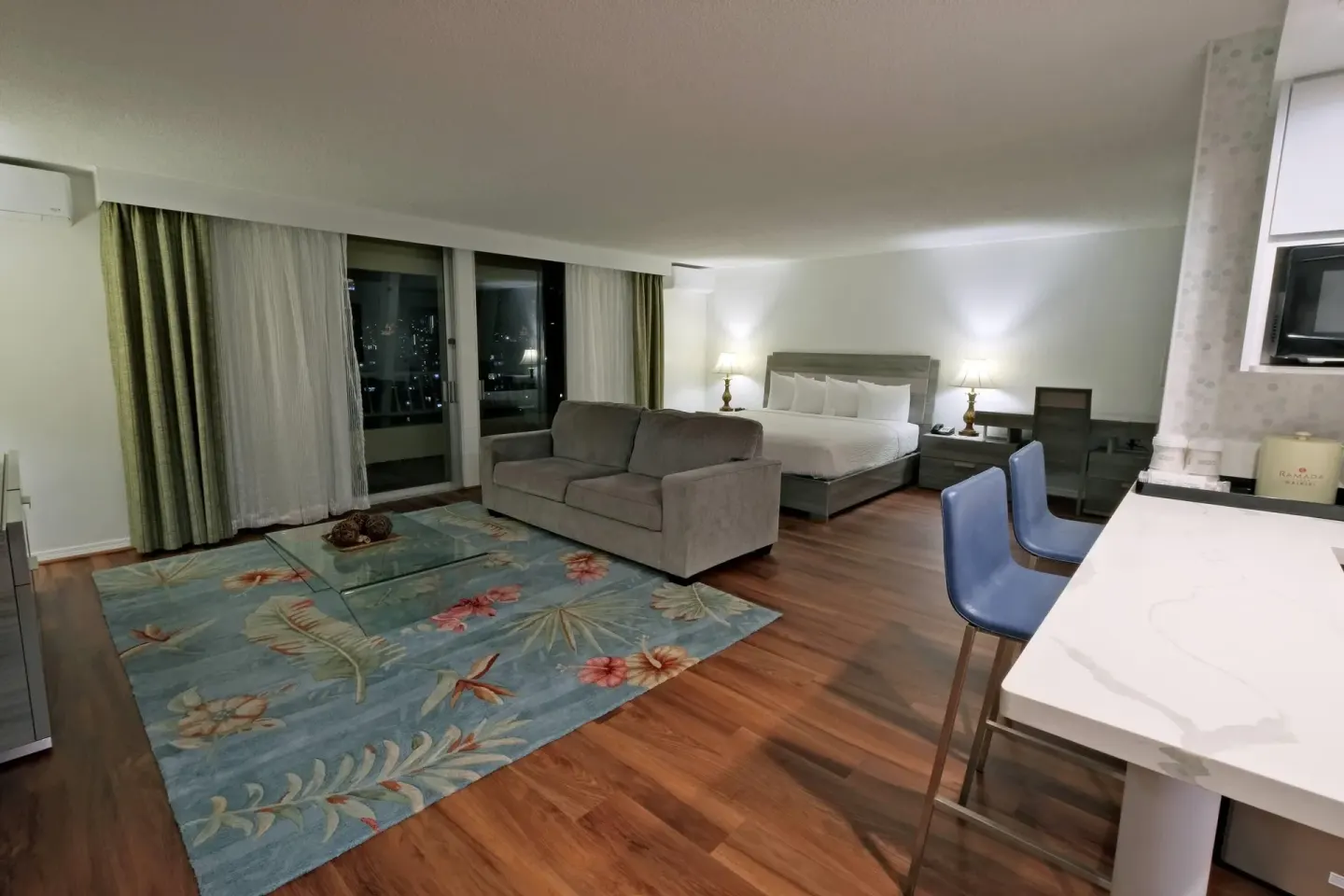 Studio suite with bed, sofa, rug, and kitchenette counter at Ramada Plaza Waikiki.