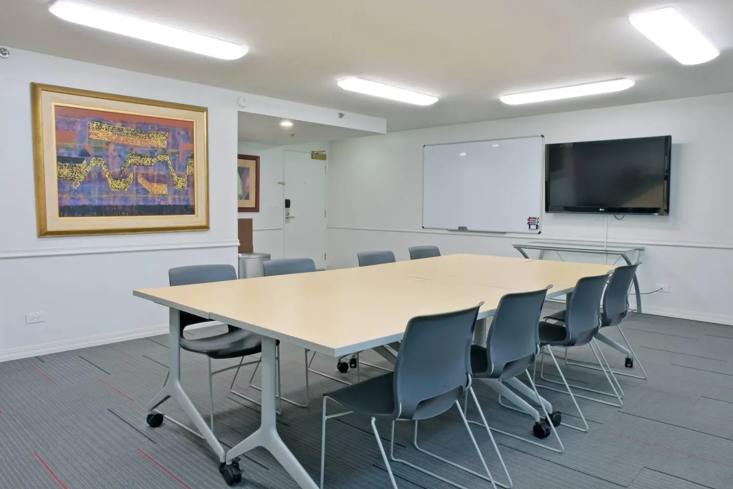 Meeting room with conference tables, chairs, whiteboard, and TV at Ramada Plaza Waikiki.