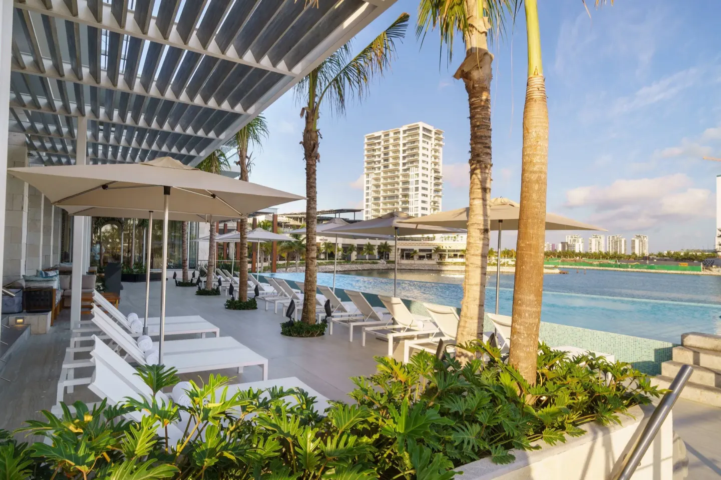 Pool deck at Renaissance Cancun Resort & Marina with loungers, umbrellas, palms, and marina views.