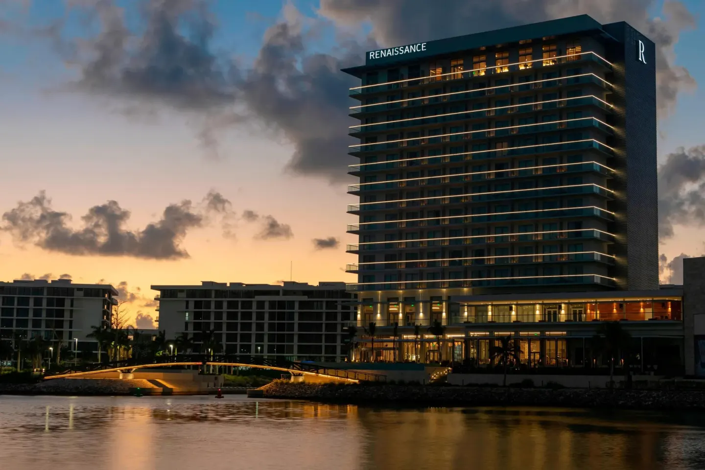 Renaissance Cancun Resort & Marina tower at dusk beside the water with illuminated balconies.