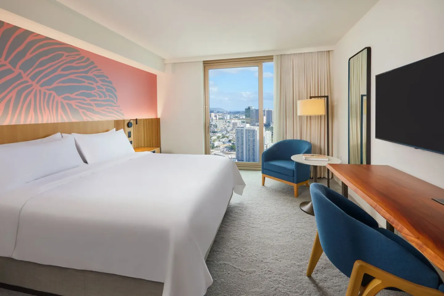 King guest room with desk, TV, blue seating, and skyline view at Renaissance Honolulu Hotel & Spa.