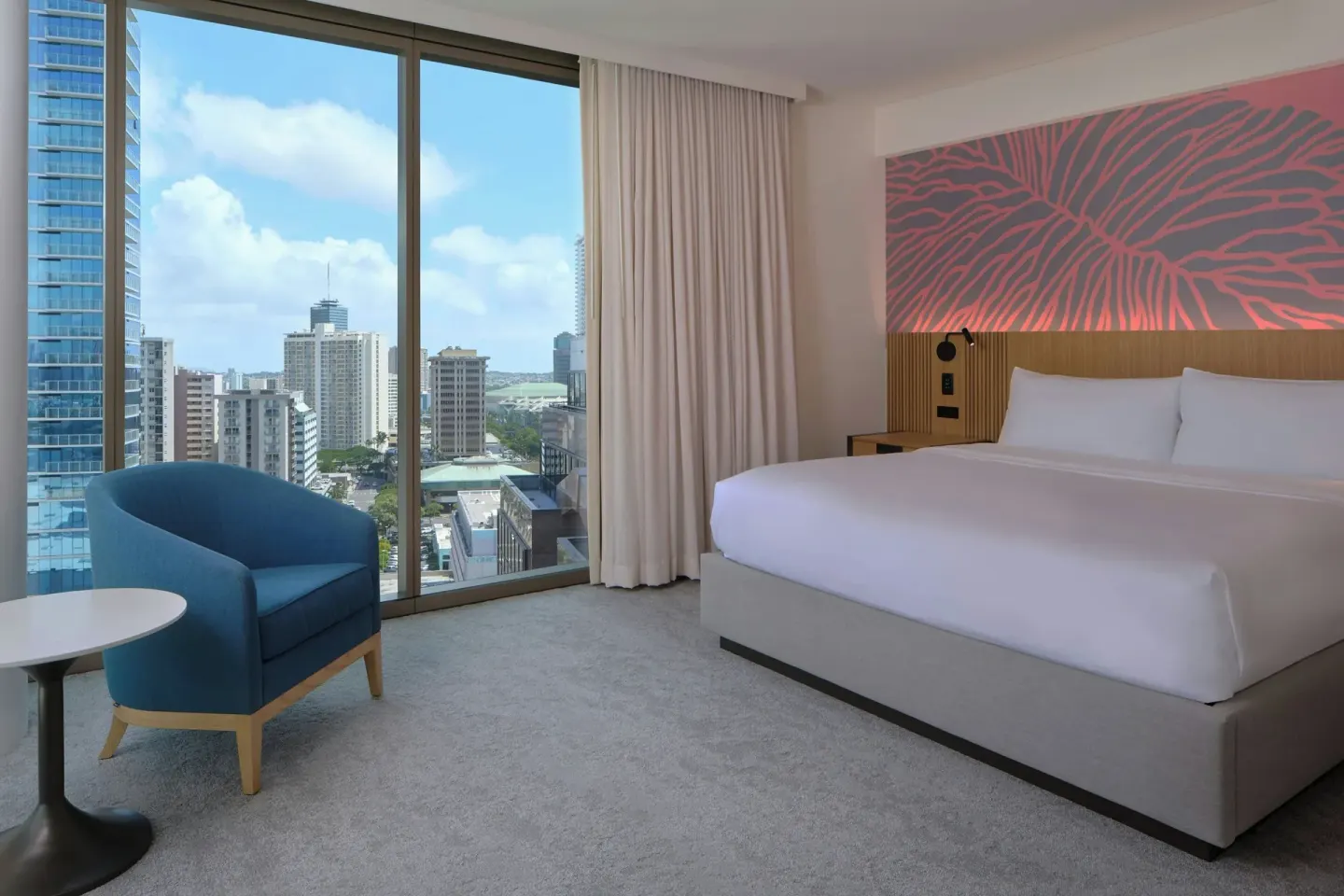 King guest room with blue chair and floor-to-ceiling city window at Renaissance Honolulu Hotel & Spa.