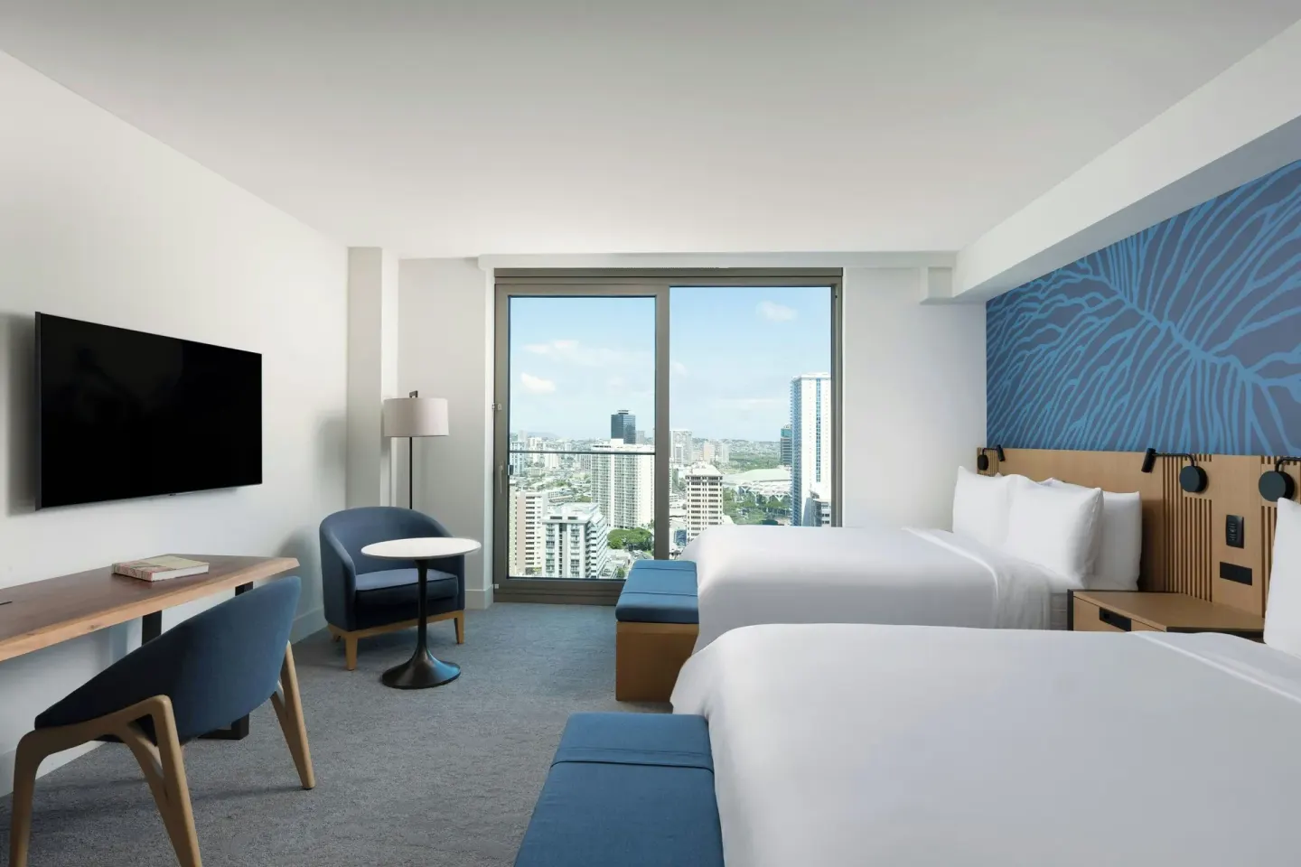 Two-bed guest room with desk, TV, seating, and city window at Renaissance Honolulu Hotel & Spa.