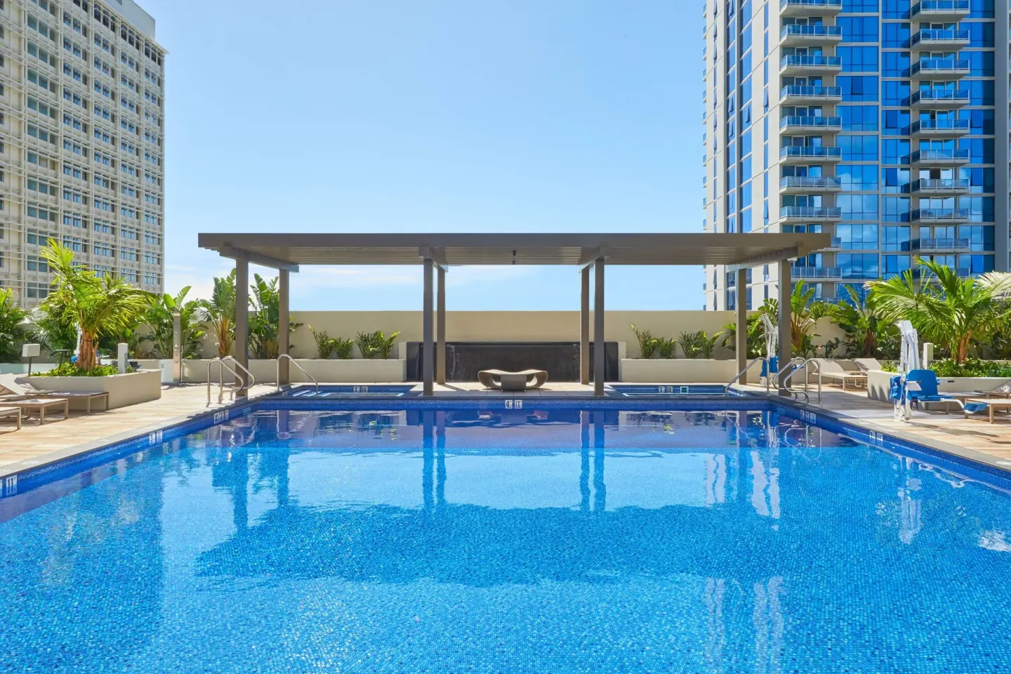 Rooftop pool deck with lounge chairs and city towers at Renaissance Honolulu Hotel & Spa.